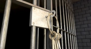 A closeup of the lock of a jail cell with iron bars and a bunch of key in the locking mechanism with the door open