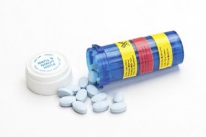 Blue prescription bottle with side effects stickers and blue pills.