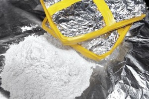 Two bricks of cocaine wrapped in foil beside a heap of cocaine.