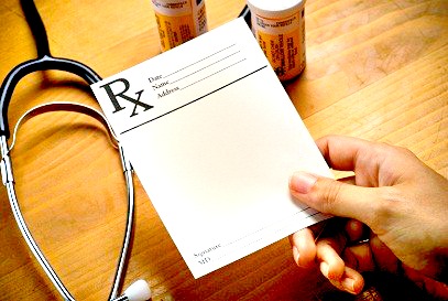 hand holding prescription pad with stethoscope and pill bottles on desk